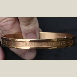 Metalarmbnd i bronce med slogan "to travel is to live". Sm brugsspor. Diameter 6,5cm.